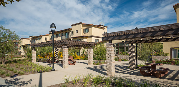 Outdoor gathering space with pergolas, landscaping, lighting, and seating areas.